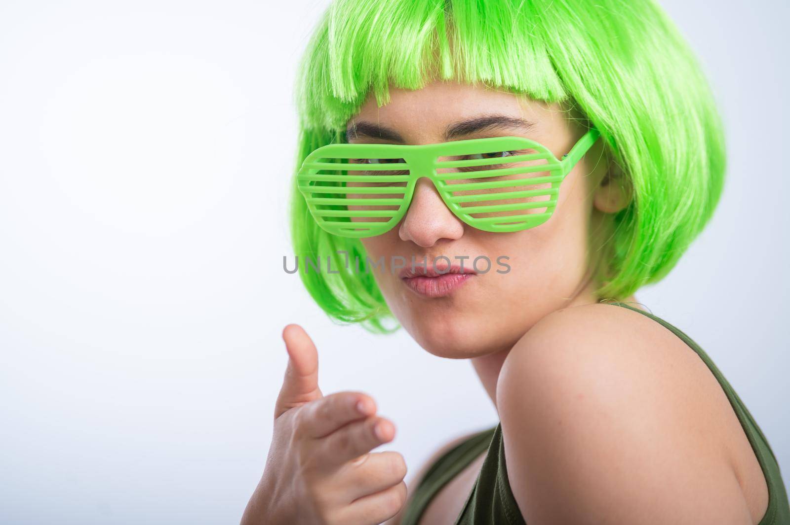 Cheerful young woman in green wig and funny glasses celebrating st patrick's day on a white background.