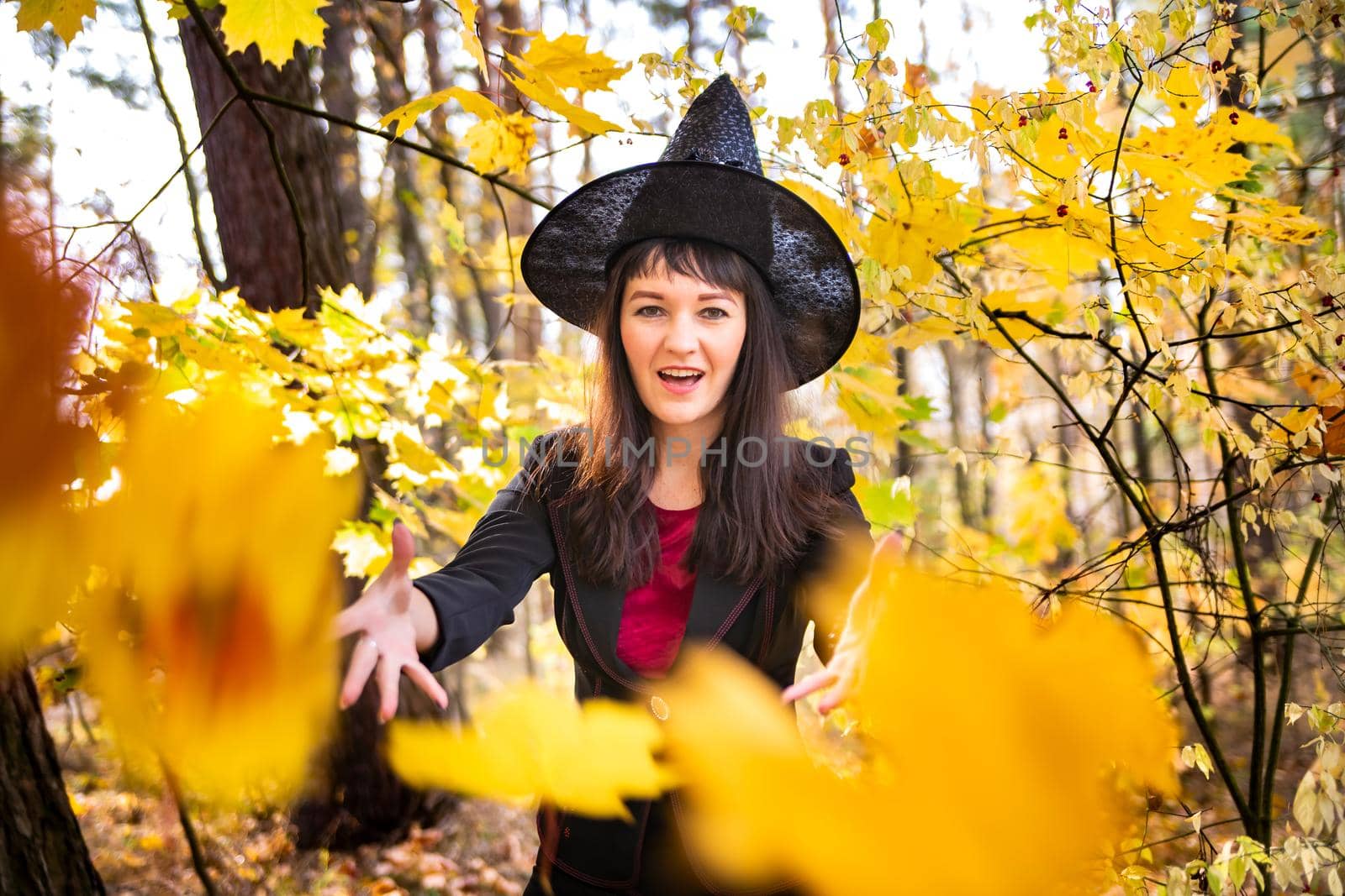 attractive witch in the autumn forest conjures. yellow fallen maple leaves on the background