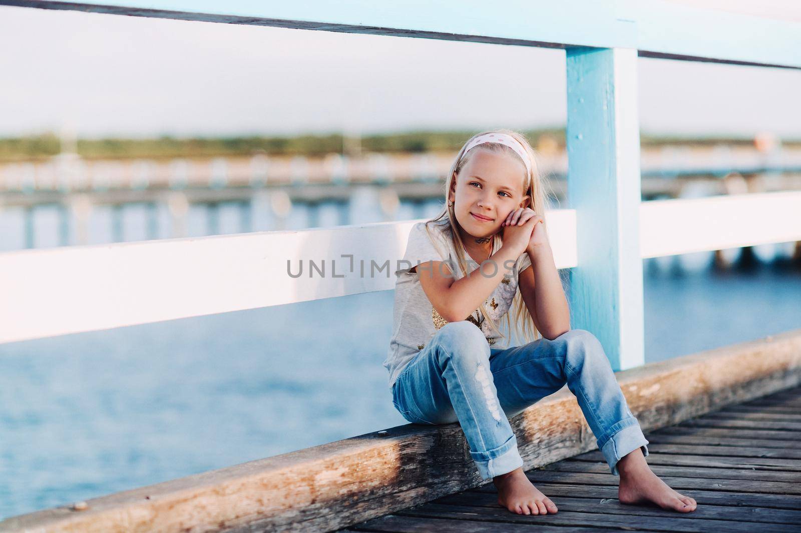 Portrait of a happy little girl sitting on a wooden bridge with sunlight.