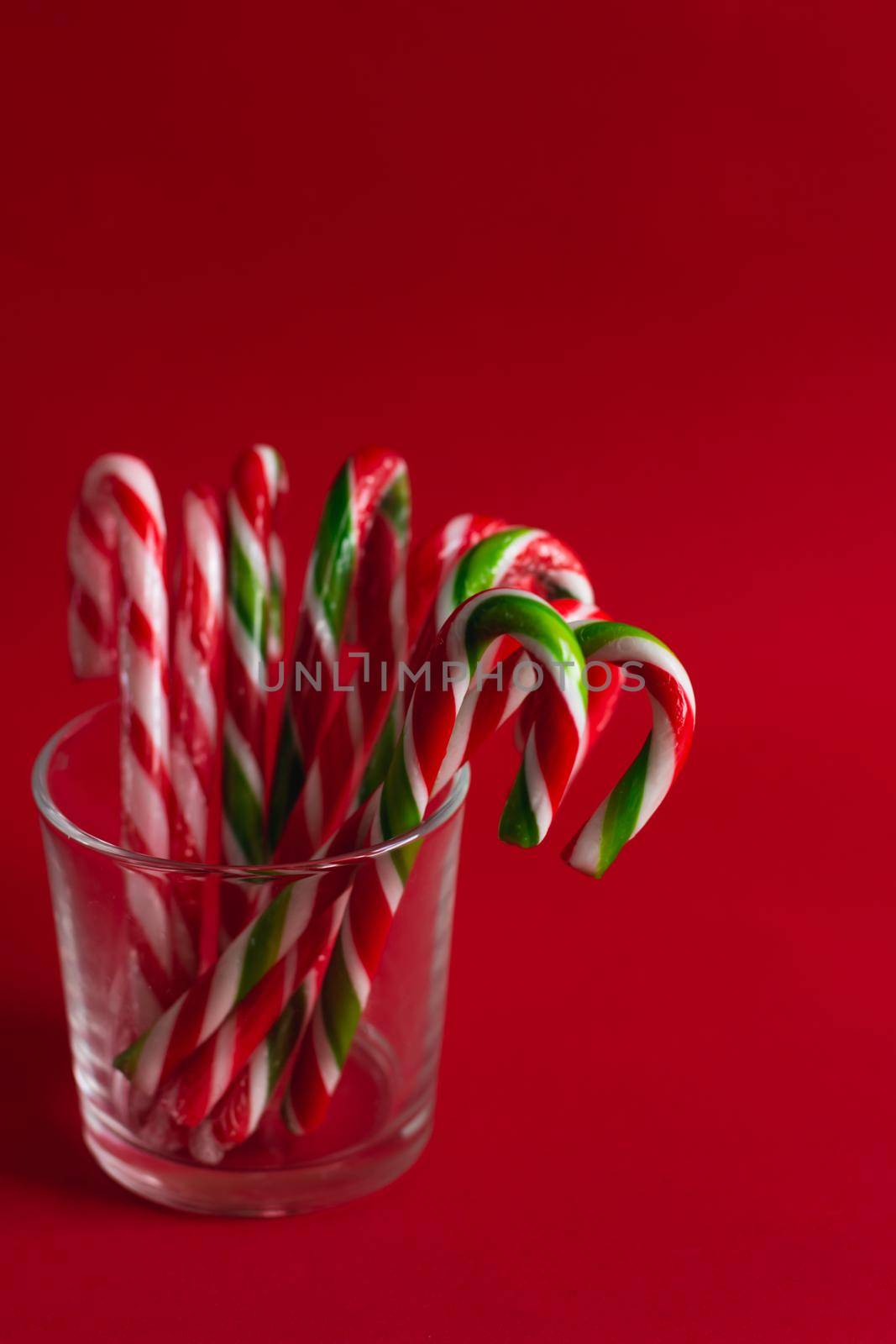 Christmas candies in the form of a cane stand in a transparent glass glass on a red background. Vertical orientation of the image. Christmas lollipops.