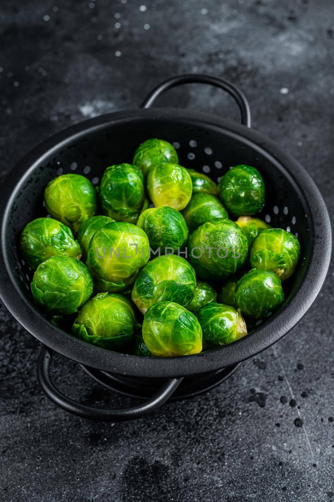 Brussels sprouts green cabbage in colander. Black background. Top view by Composter