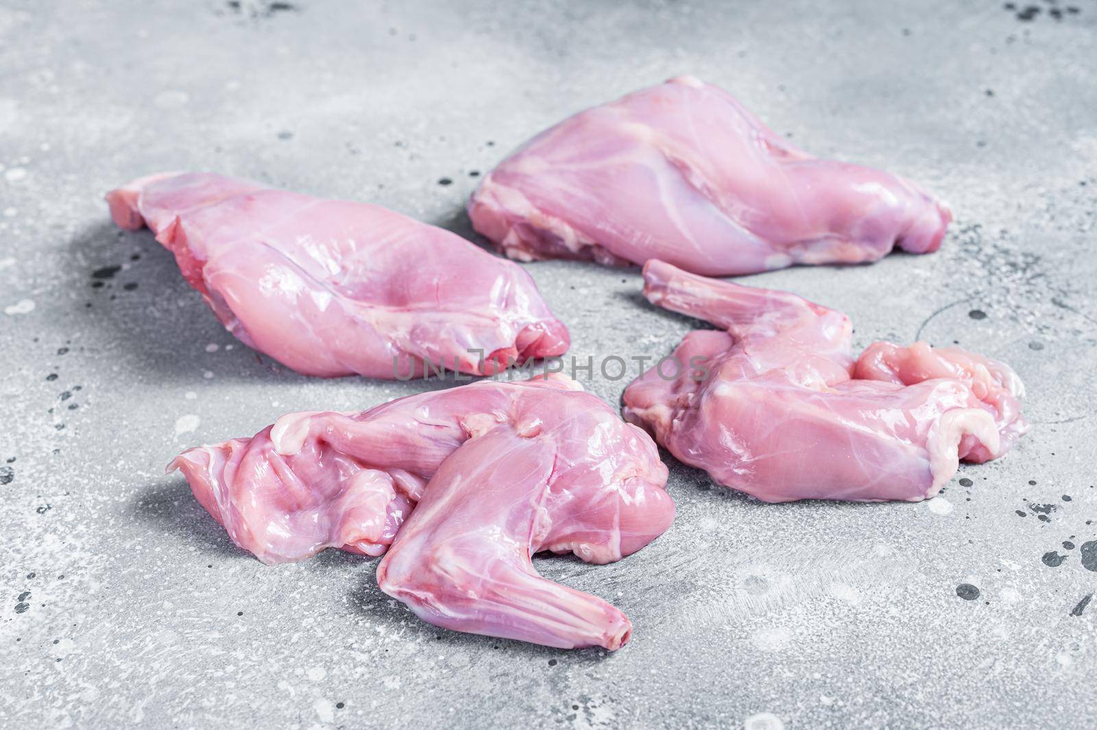 Raw rabbit legs slices on a butcher board. Gray background. Top view by Composter