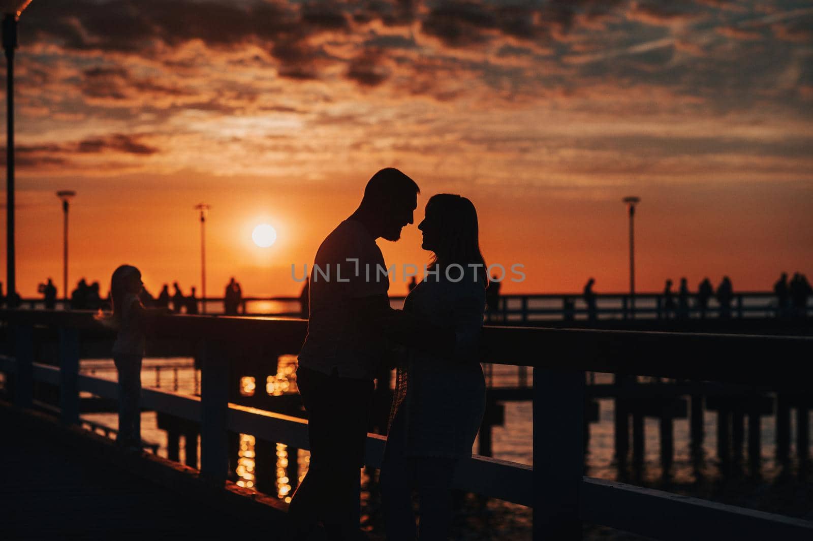 Portrait silhouette of a beautiful newlywed couple. A loving man hugs a girl at sunset, against the background of the sea standing on the pier