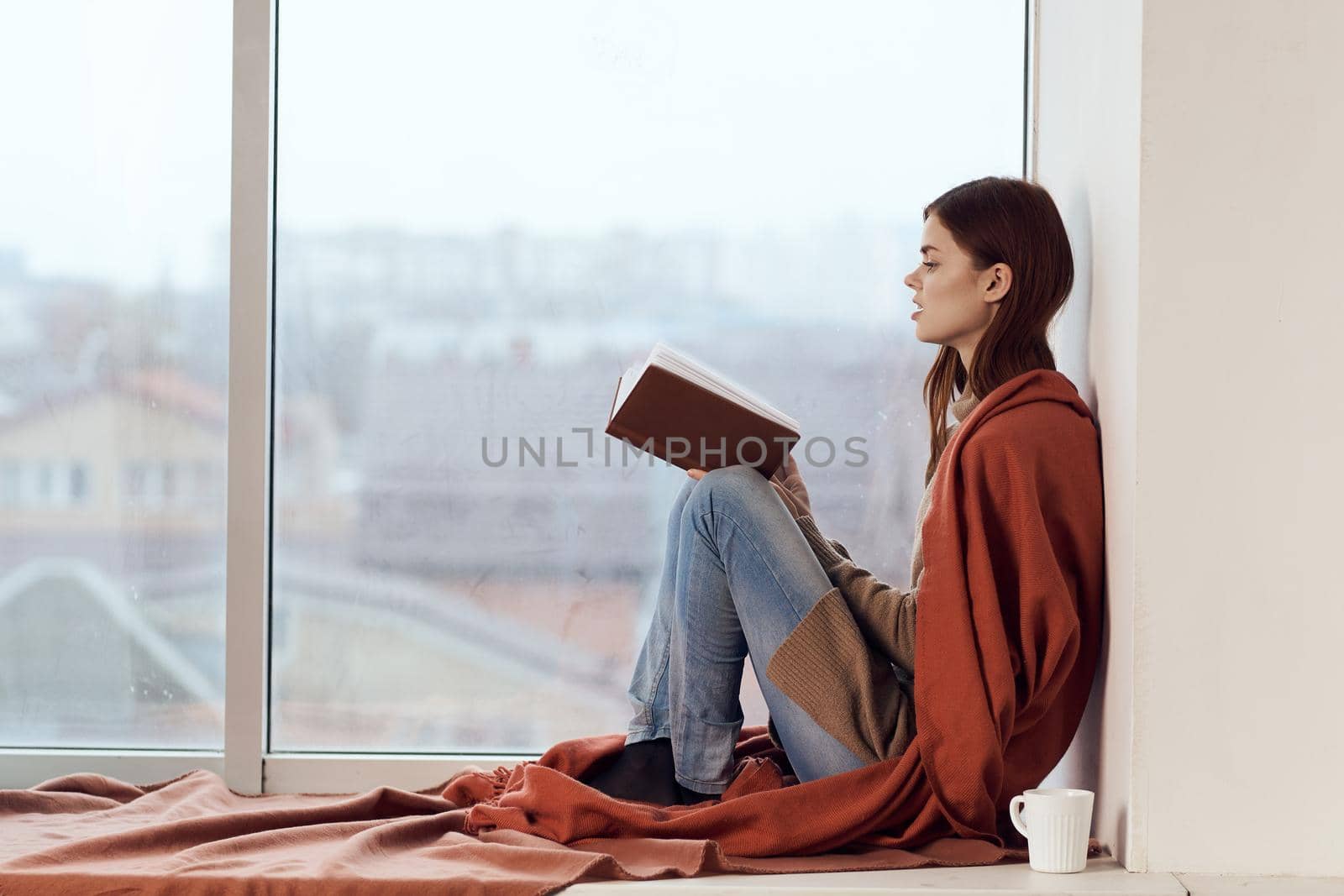 woman with a book near the window with a cup of coffee by Vichizh