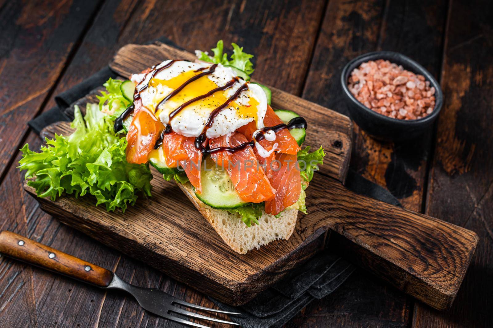 Smoked salmon Sandwich with Benedict egg and avocado on bread. Dark wooden background. Top view.