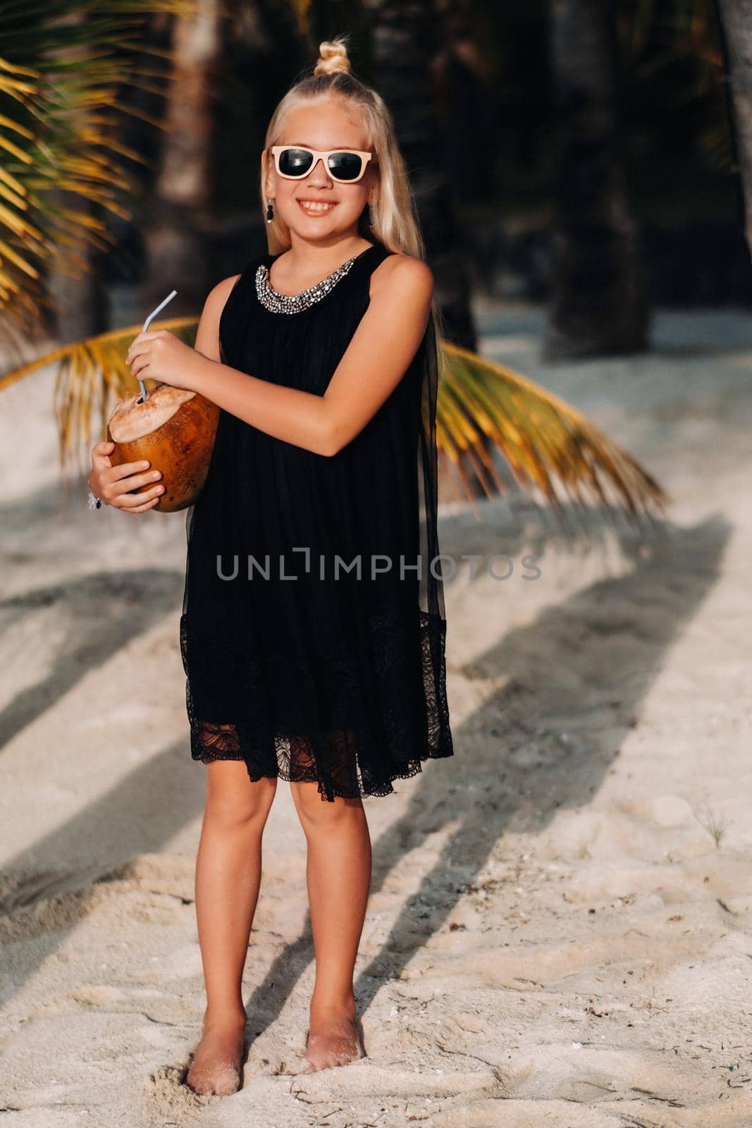 Portrait of a cheerful 9-year-old girl with a coconut cocktail on the background of palm trees on an exotic beach.little Girl with a coconut on the beach of the island of Mauritius.