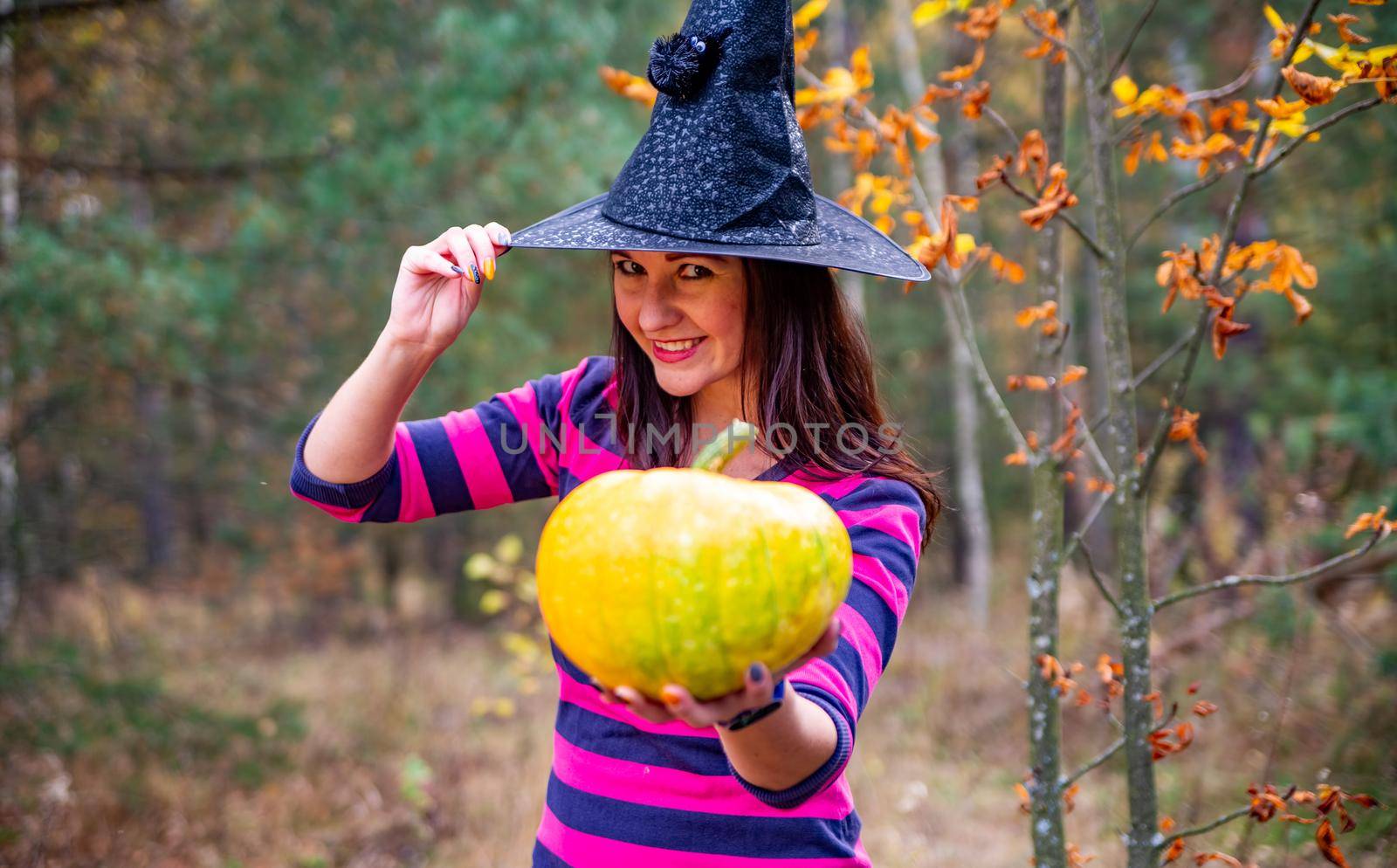 Halloween warm beautiful witch with pumpkin in autumn forest