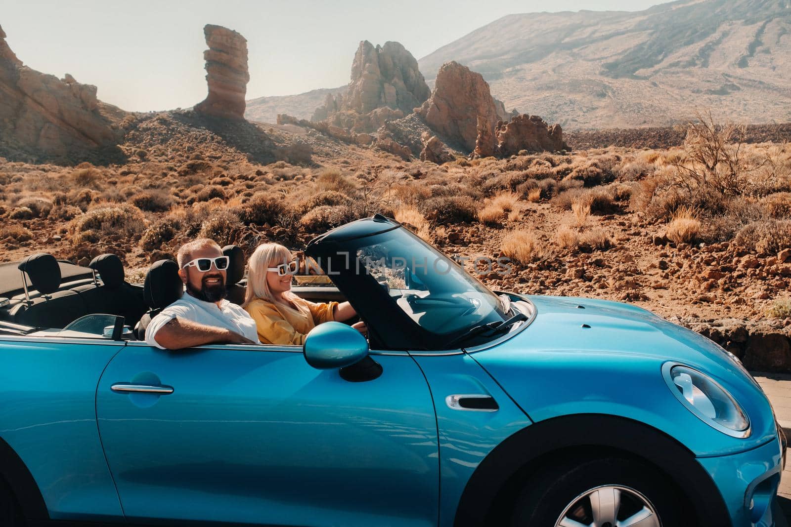 a woman and a man wearing glasses in a convertible car on a trip to the island of Tenerife. The crater of the Teide volcano, Canary Islands,Spain.