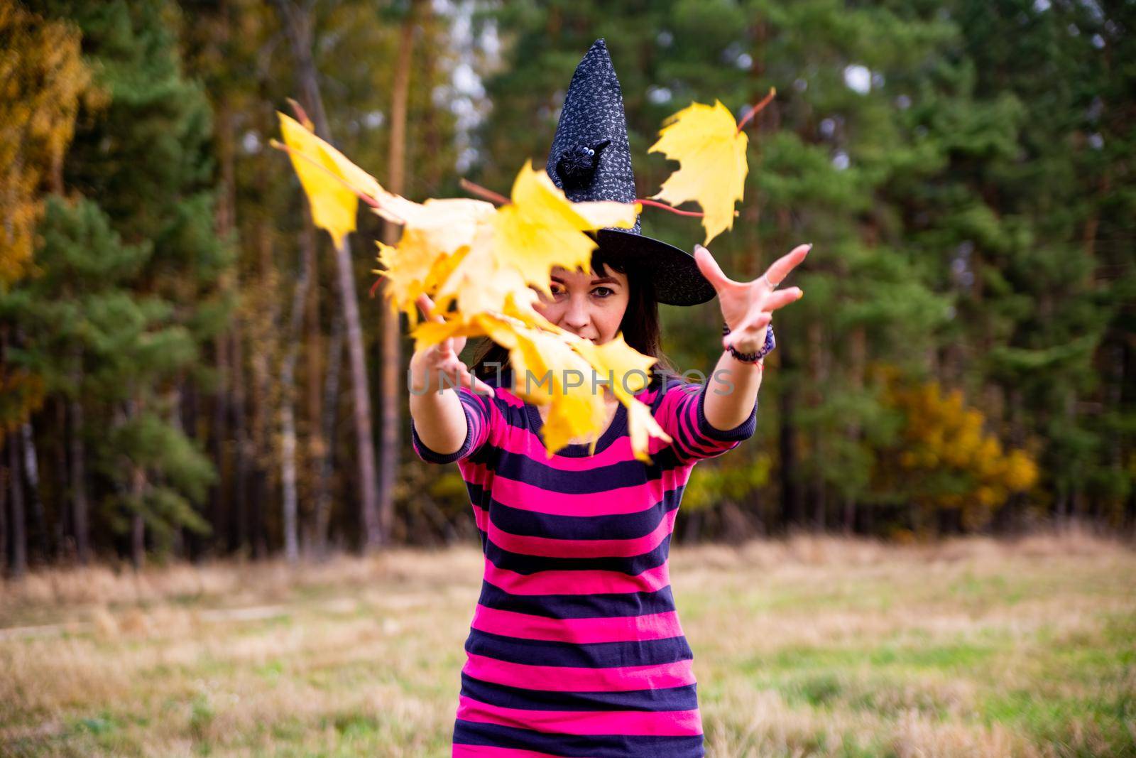 witch throws leaves in the autumn forest. Halloween costume party magician woman