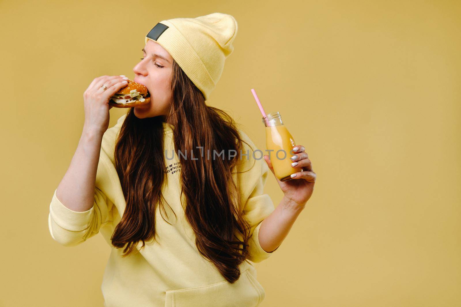 pregnant girl in yellow clothes with hamburgers in her hands on a yellow background.