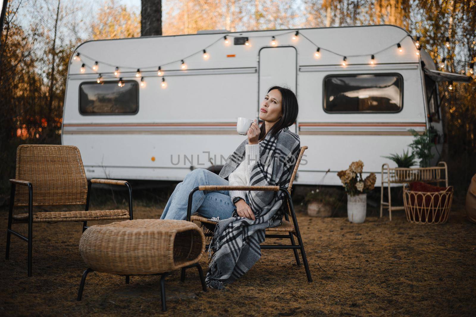 Beautiful caucasian woman is sitting wrapped in a plaid and drinking a warming drink outdoors. Traveling in a motor home in autumn. by mrwed54