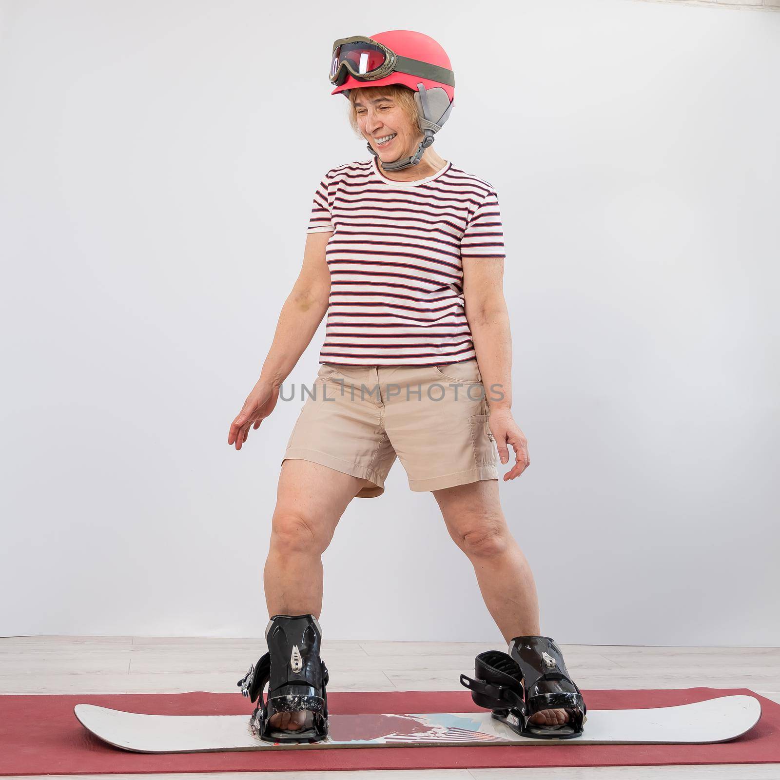 Elderly woman imitates snowboarding in the studio on a white background