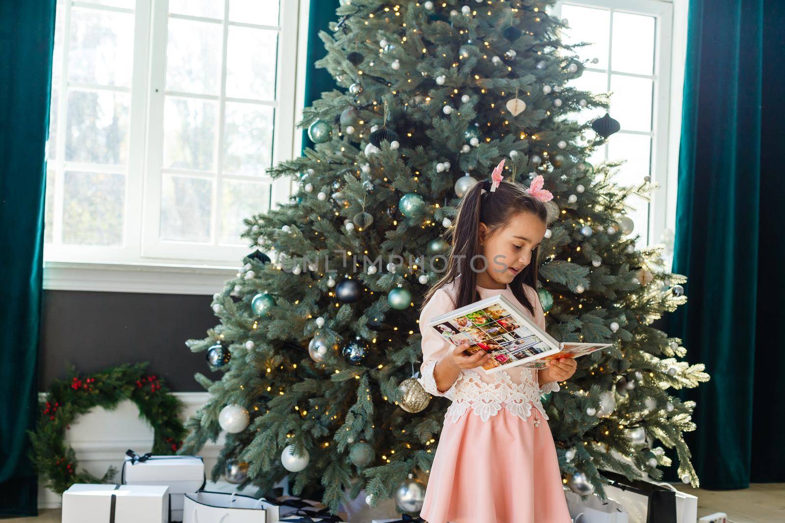 little girl looking photobook in front of Christmas tree