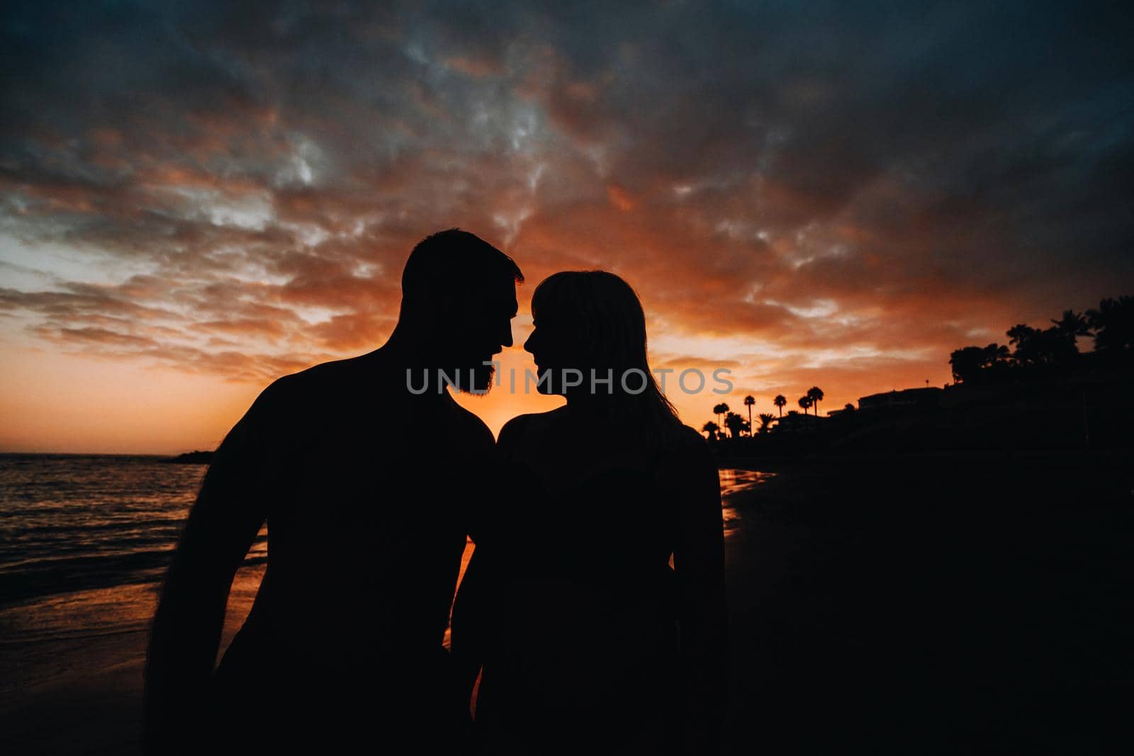Romantic couple on the beach in a colorful sunset in the background.A guy and a girl at sunset on the island of Tenerife by Lobachad