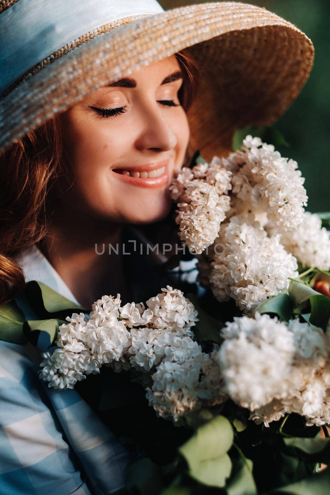 Portrait of a beautiful girl with long hair, a straw hat and a long summer dress with lilac flowers in the garden.