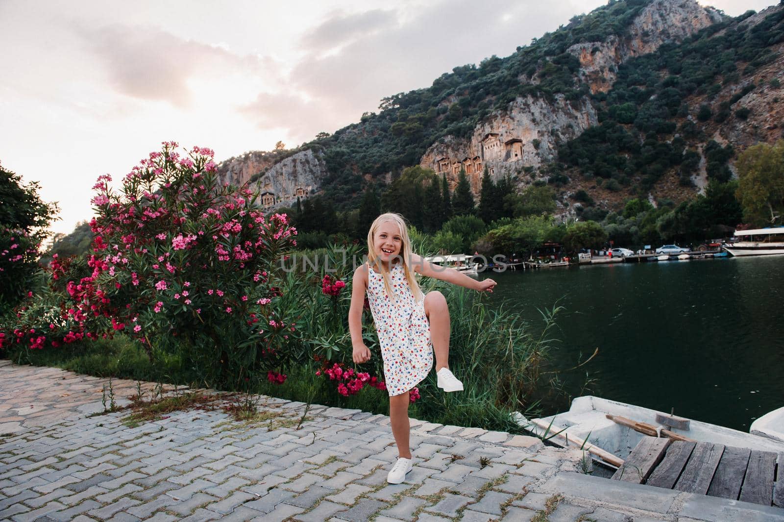 Photo of a pretty funny excited little girl by the river in a white sundress