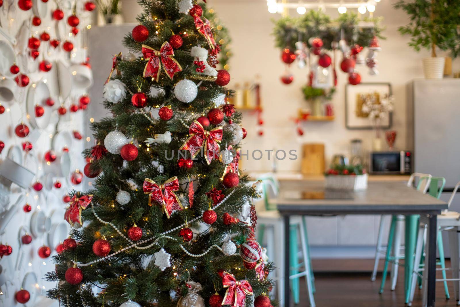beautiful home interior of kitchen decoreted for christmas celebration. red decorated christmas tree on foreground. no people by Mariaprovector