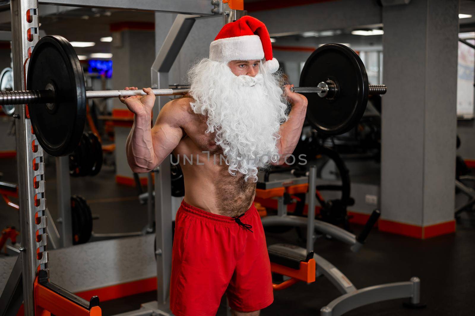 Santa claus in the gym. Muscular man with a naked torso doing exercises with dumbbells. by mrwed54