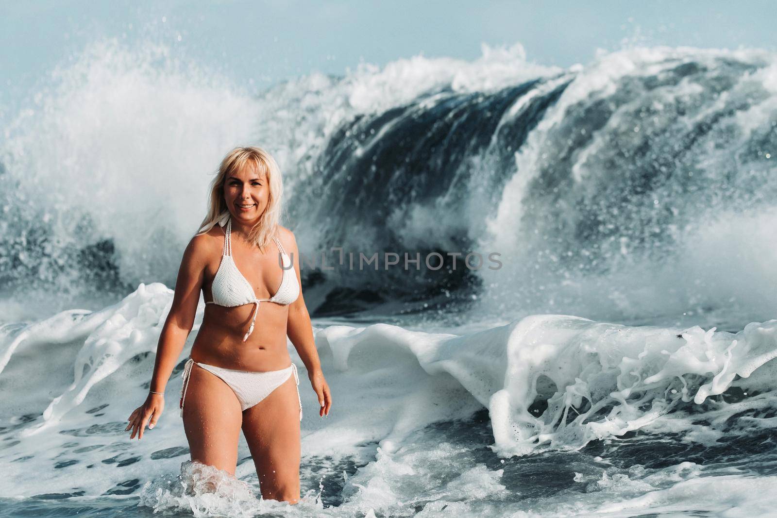 A girl with wet hair jumps over large waves in the Atlantic ocean, around a wave with splashes of spray and water drops.Tenerife.Spain.