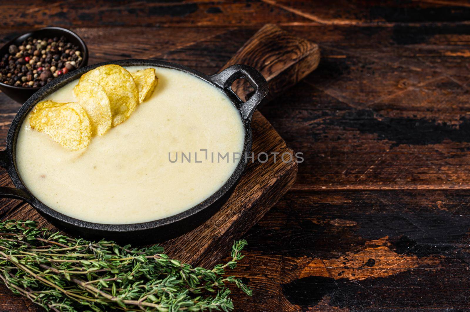 Potato cream soup with potato chips in pan on wooden board. Dark wooden background. Top view. Copy space.