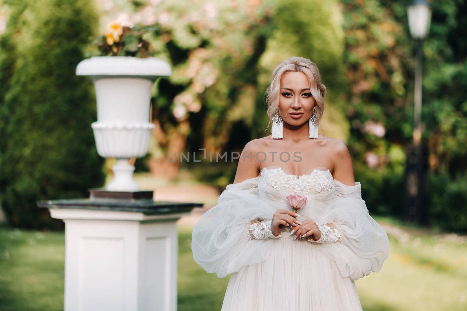 A beautiful bride in a luxurious wedding dress holds a rose and greenery on a green natural background. Portrait of a happy bride in a white dress, smiling against the background of a Park