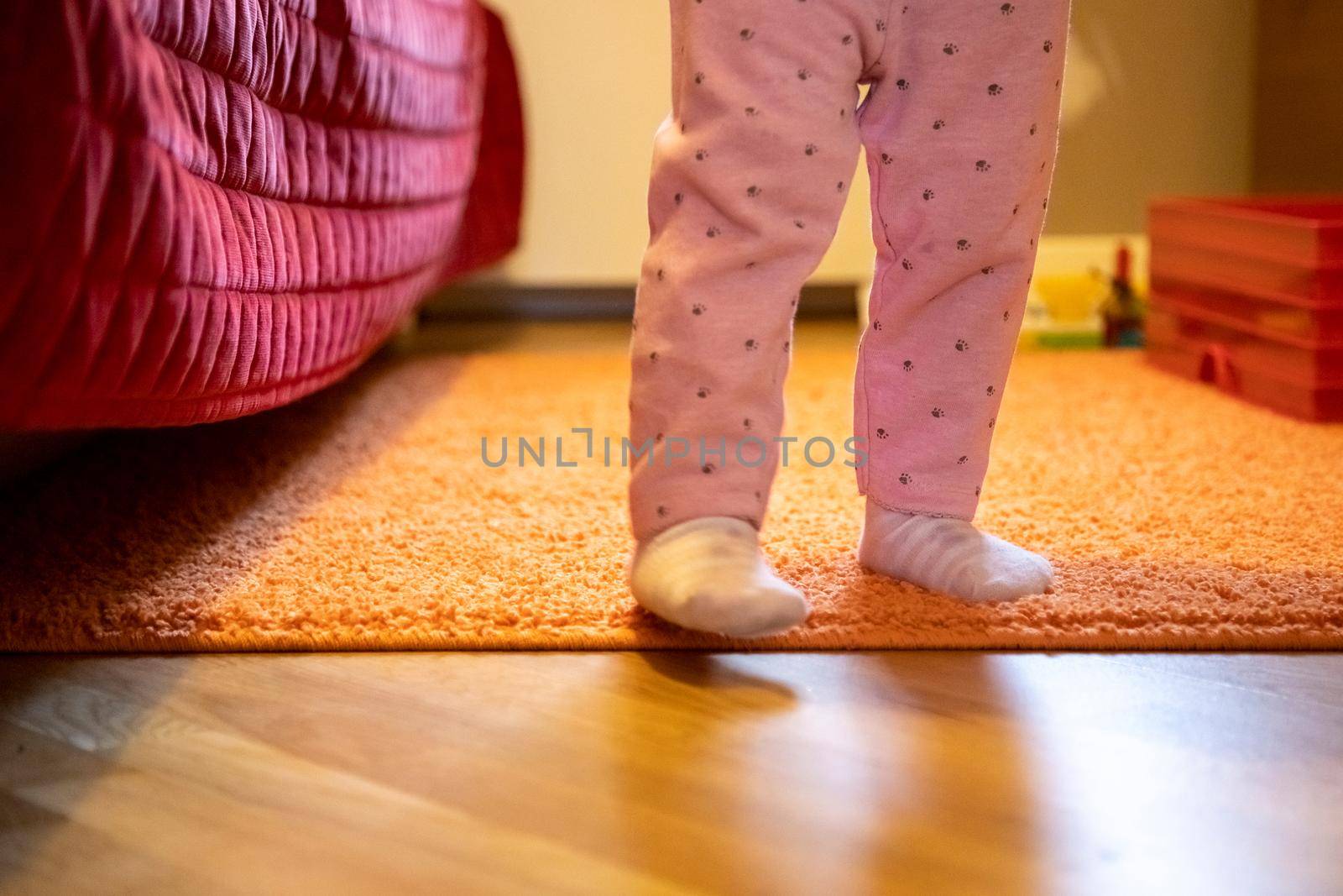 the legs of a small child are walking around the room. baby's first steps concept. no face. happy parenthood