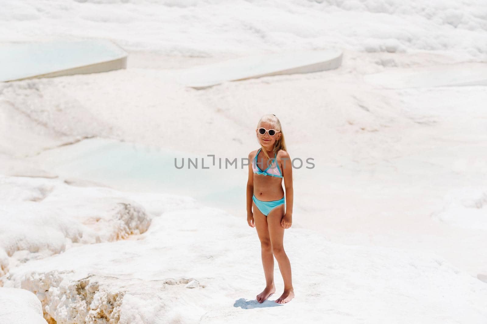 little girl in a swimsuit and sunglasses on White mountain, Sunny summer day, Pamukkale, Turkey.