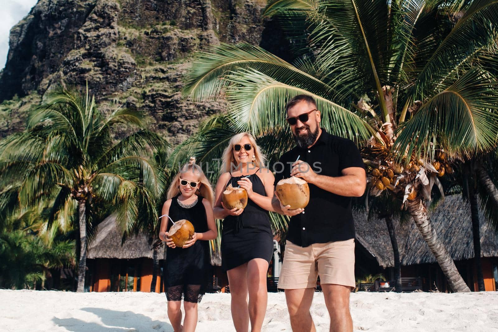 a stylish family in black clothes with coconuts in their hands on the beach of the island of Mauritius.Beautiful family on the island of Mauritius in the Indian ocean by Lobachad