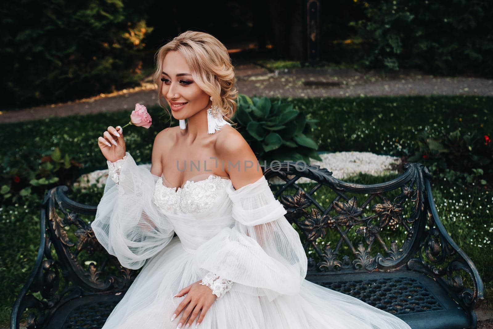 Bride's morning in the garden. Portrait of a young bride looking at her wedding dress, hanging on a garden tree