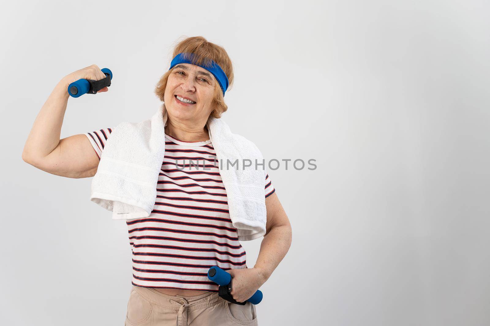 An elderly woman with a blue bandage on her head trains with dumbbells on a white background by mrwed54