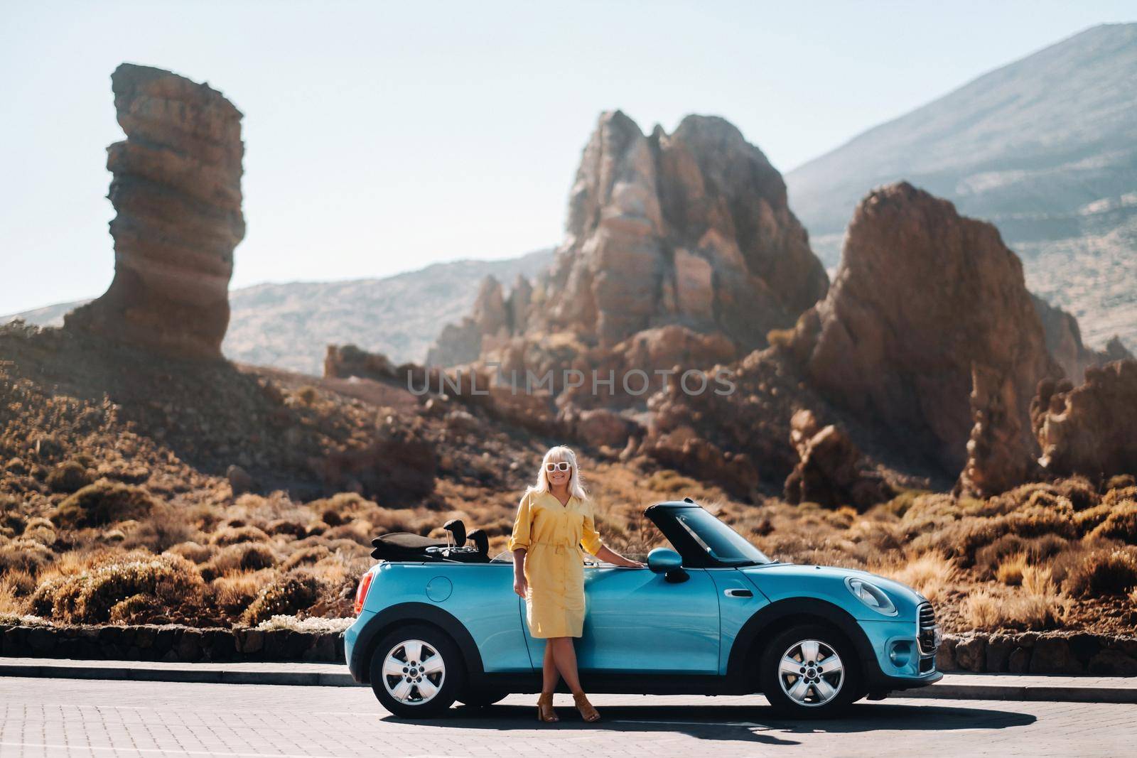 Girl in yellow dress enjoying a road trip in a convertible through a deserted valley with mountains, Canary Islands, Tenerife. by Lobachad