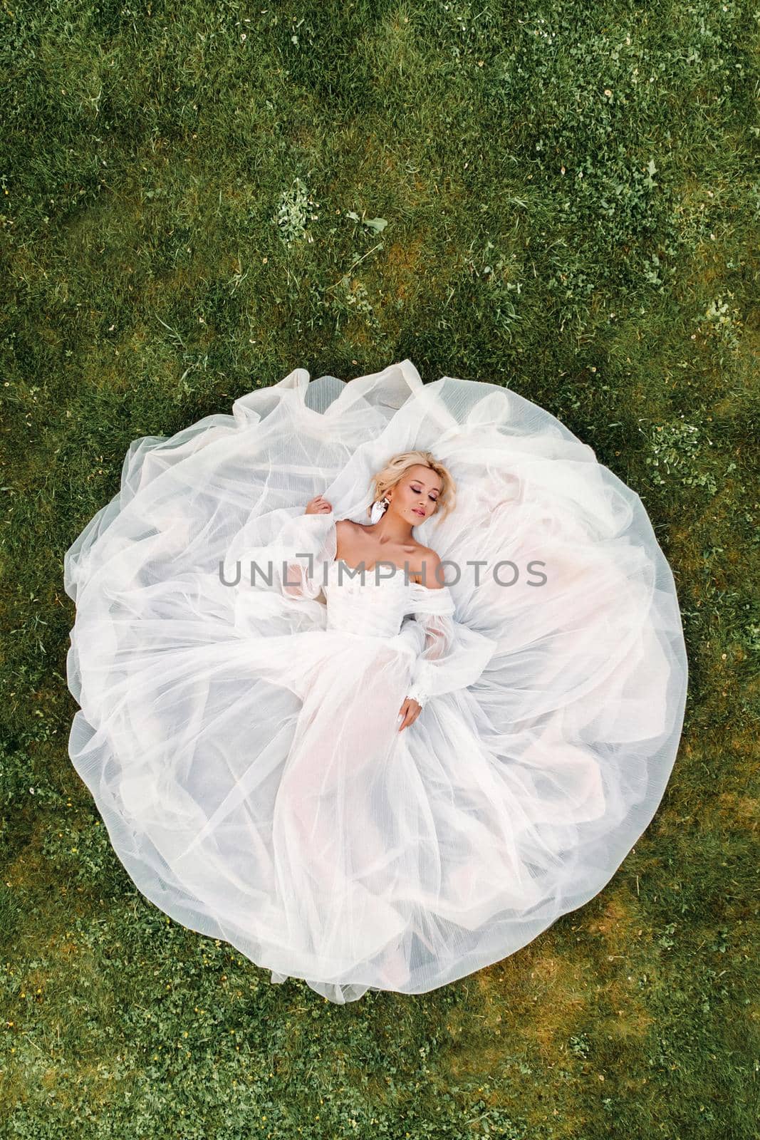 Portrait of a beautiful bride lying on the ground in a white wedding dress.photo of an elegant bride on the green grass.Top photo of the bride by Lobachad