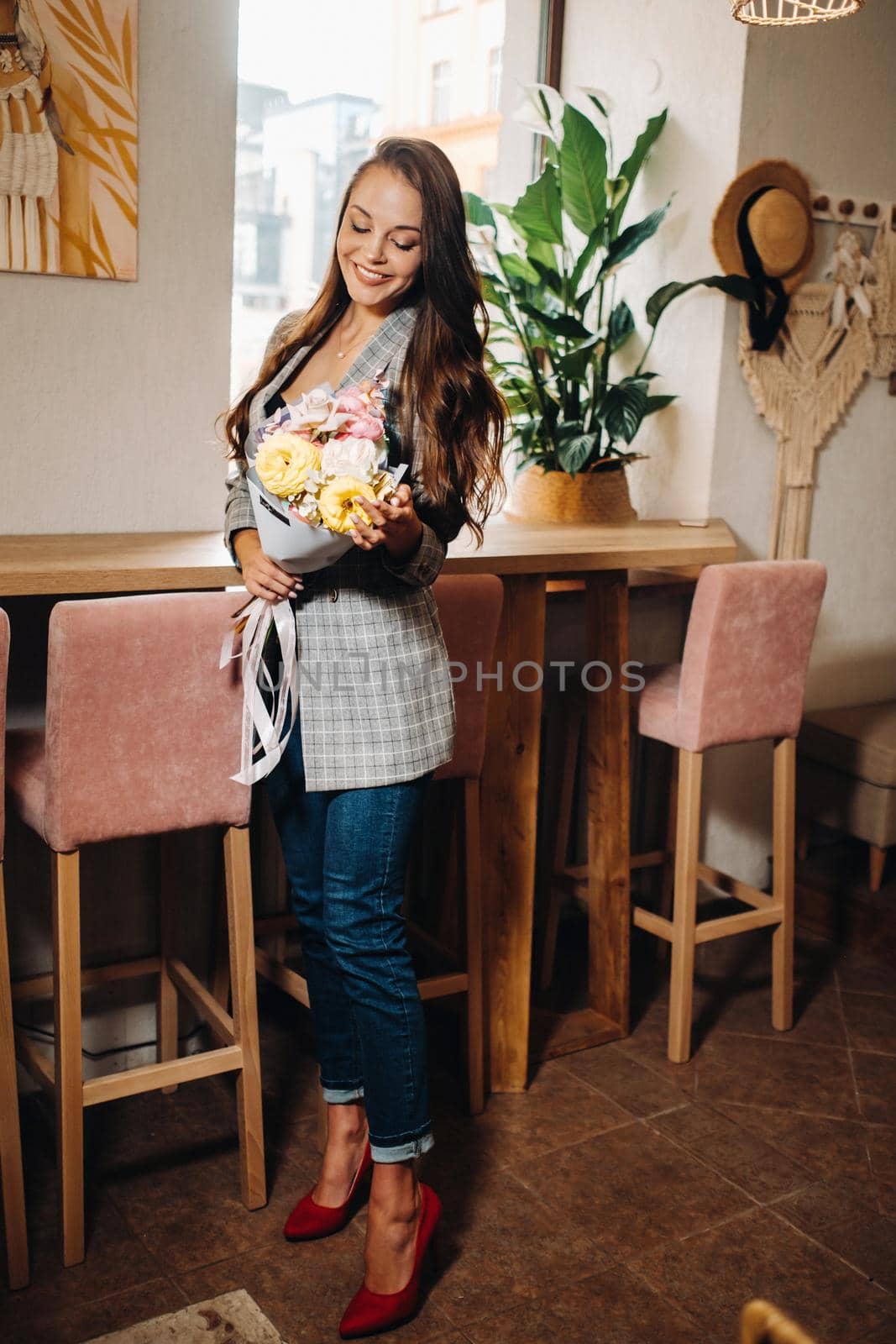 Portrait of a young European girl with long hair in a cafe with a bouquet standing near the window, a tall girl in a jacket with long hair in a cafe waiting.