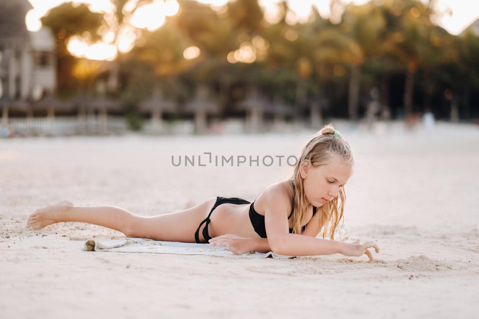 A charming little girl is lying on the beach and drawing on the sand.A little girl lies on the beach of the island of Mauritius by Lobachad