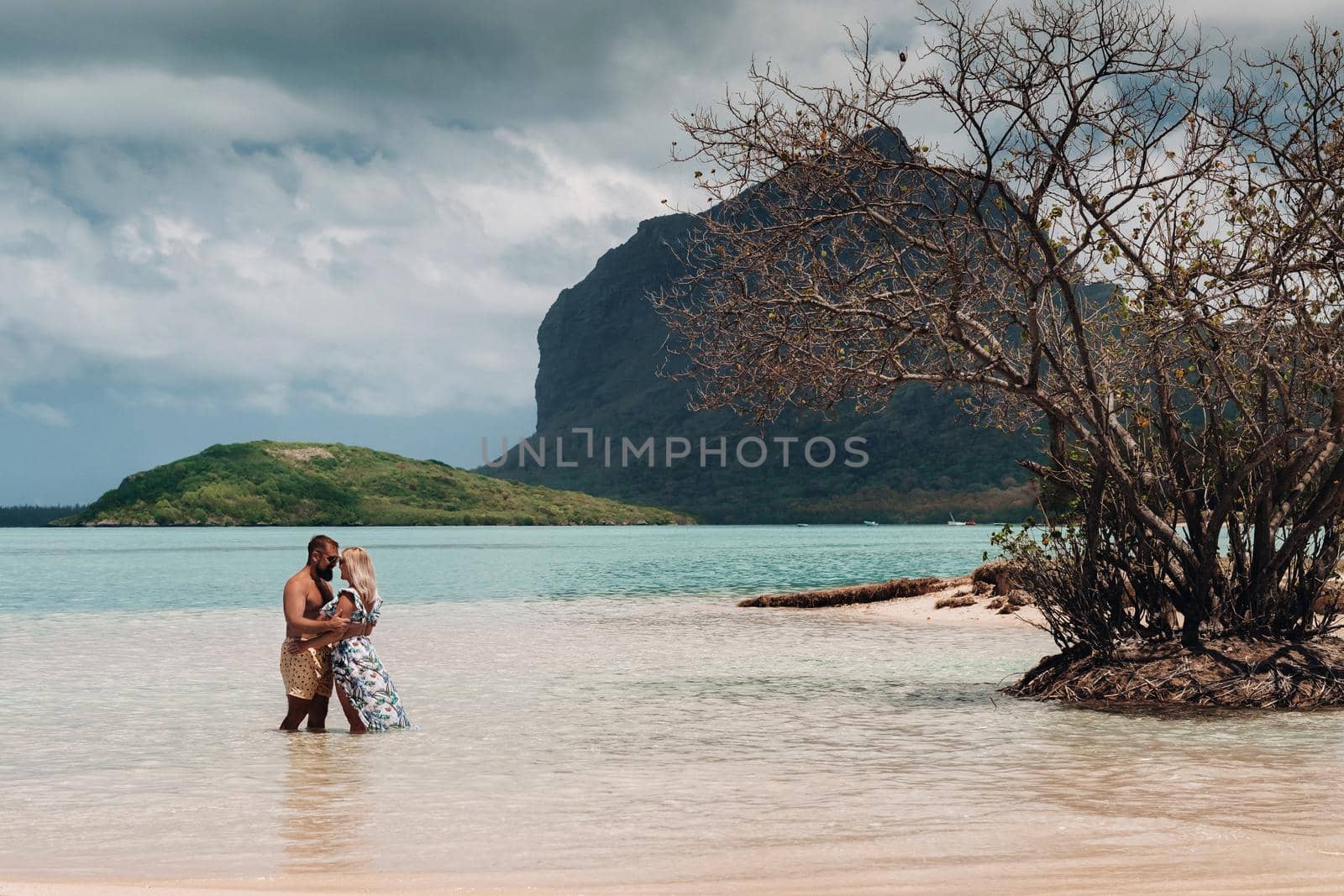 A girl in a swimsuit and a man in shorts stand in the ocean against the backdrop of mount Le Morne on the island of Mauritius.A couple in the water look into the distance of the ocean against the background of mount Le Morne Brabant by Lobachad