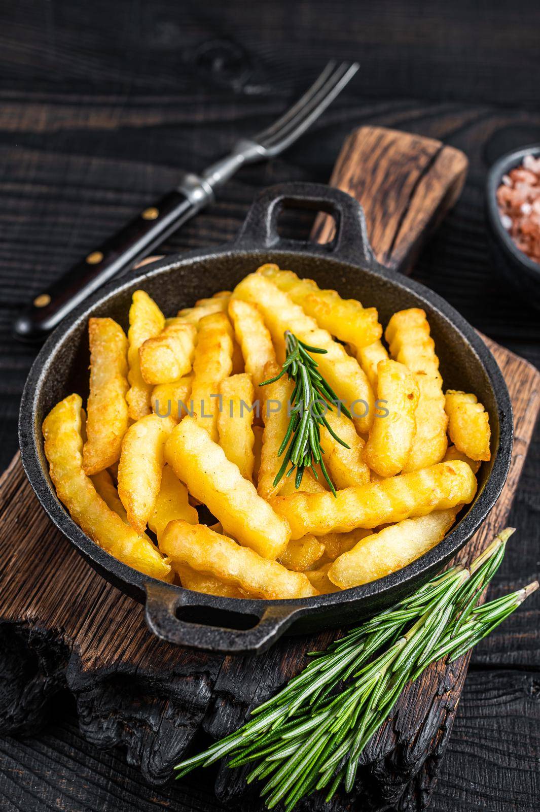 Fried Crinkle French fries potatoes in a pan. Black Wooden background. Top view by Composter