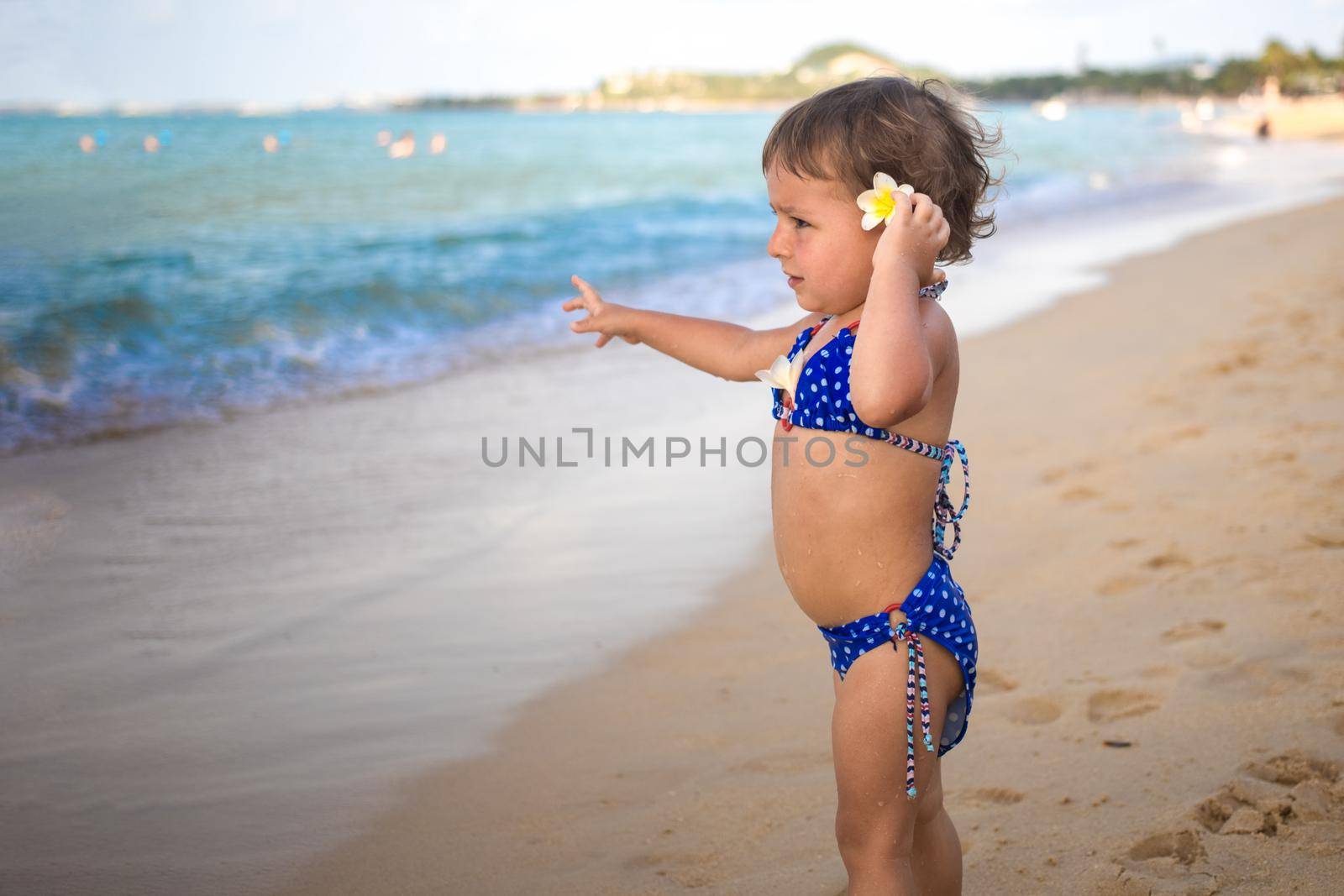 adorable toddler toddler stands on the sandy beach and points at the tropical sea. by Mariaprovector