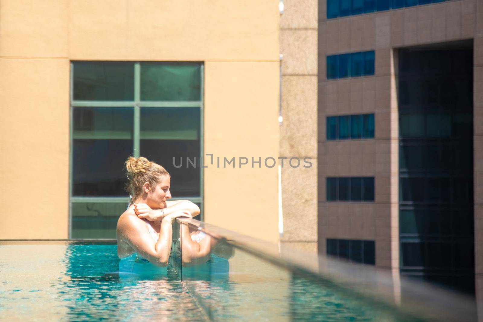 young caucasian woman relaxing in a pool on the roof of a skyscraper in a metropolis under the sun....
