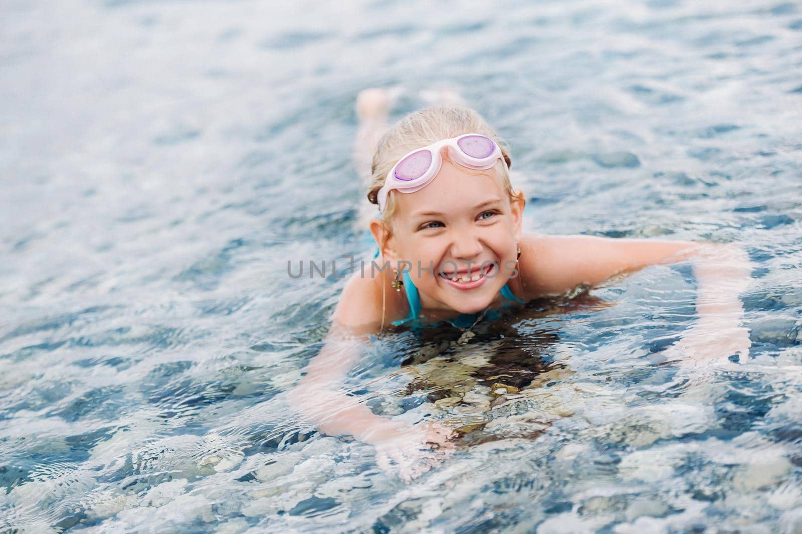 A charming little girl lies in the sea and smiles.A little girl lies in the water laughing.Turkey by Lobachad