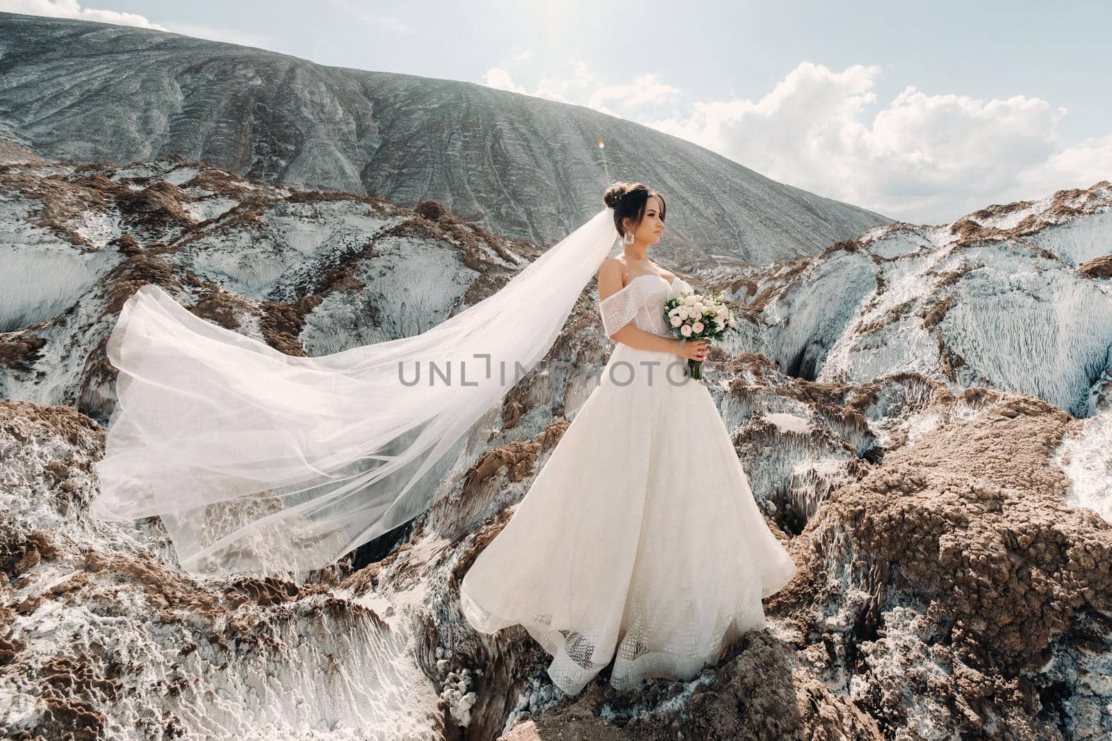 Beautiful bride in a wedding dress with a bouquet on the top of the salt mountains. A stunning young bride with curly hair . Wedding day. . Beautiful portrait of the bride without the groom. by Lobachad