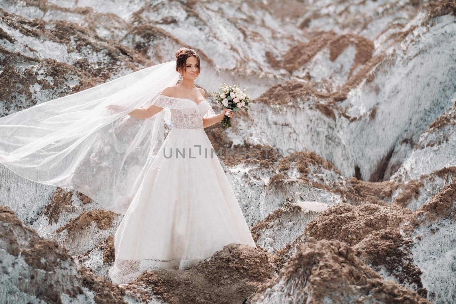 Beautiful bride in a wedding dress with a bouquet on the top of the salt mountains. A stunning young bride with curly hair . Wedding day. . Beautiful portrait of the bride without the groom by Lobachad