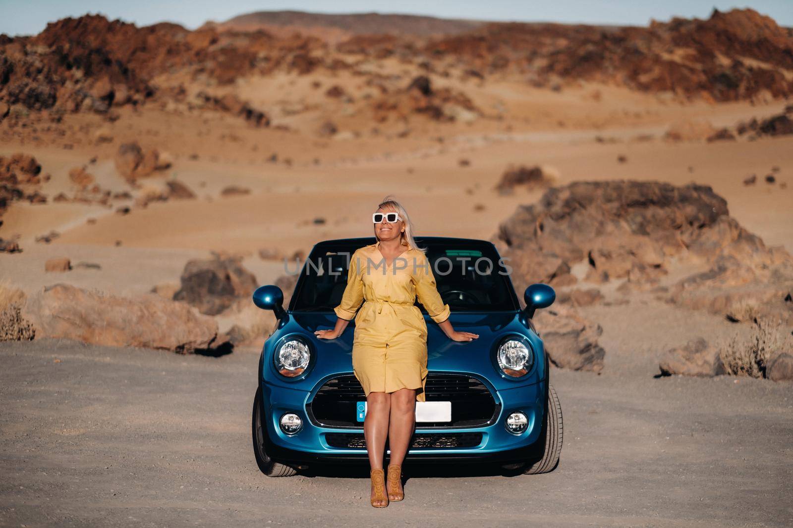 Girl in yellow dress enjoying a road trip in a convertible through a deserted valley with mountains, Canary Islands, Tenerife. by Lobachad