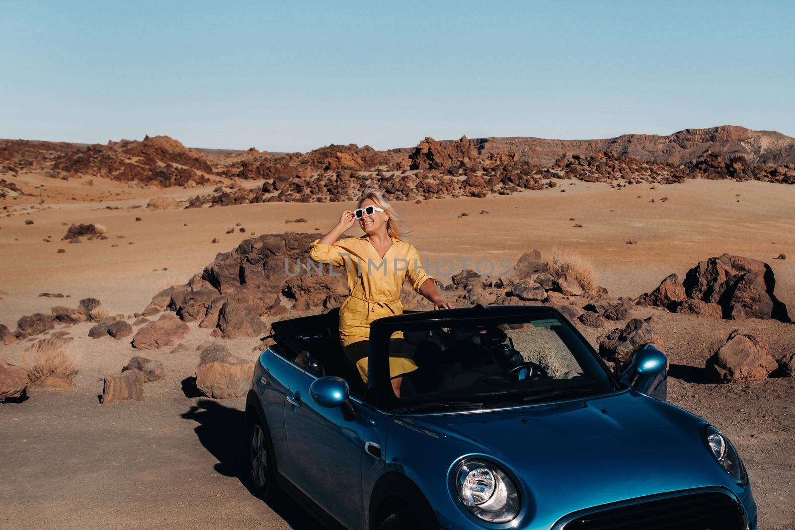 Girl in yellow dress enjoying a road trip in a convertible through a deserted valley with mountains, Canary Islands, Tenerife. by Lobachad