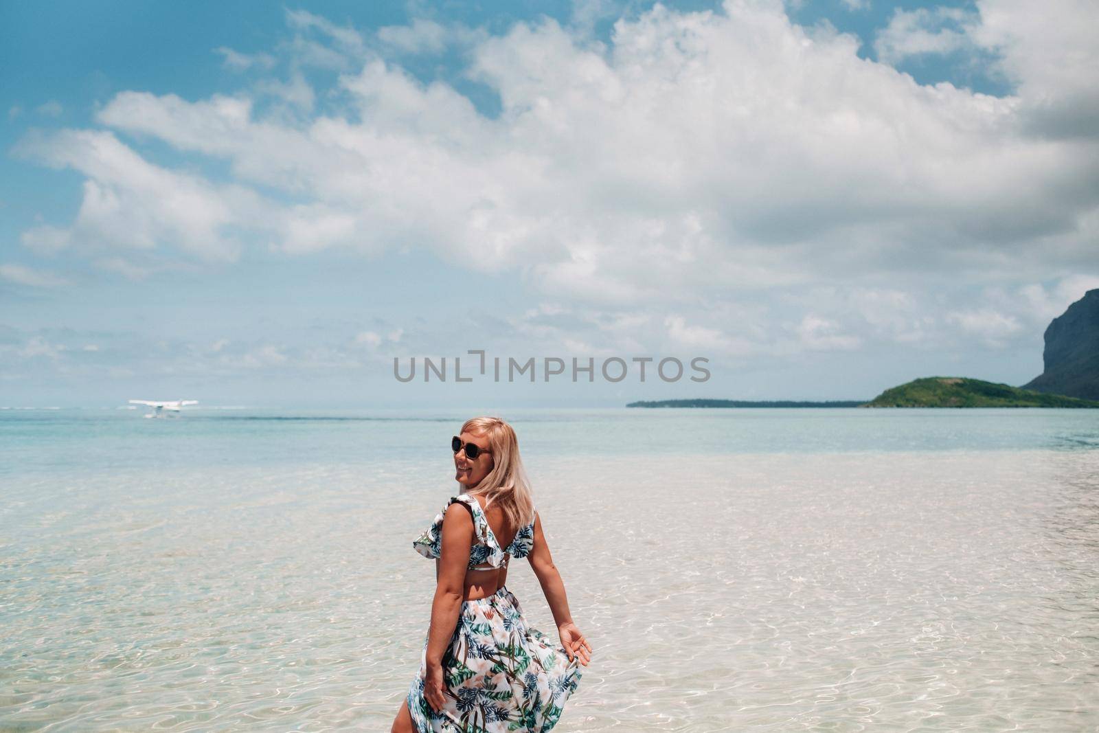 A girl in a swimsuit stands in the ocean and waits for a seaplane against the background of mount Le Morne on the island of Mauritius.A woman in the water looks back at a plane landing on the island of Mauritius.