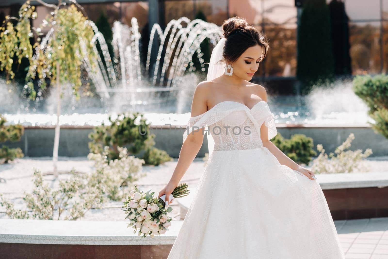 Portrait of the bride in the city near the fountain.A stunning young bride with curly hair . Wedding day. . Beautiful portrait of the bride without the groom