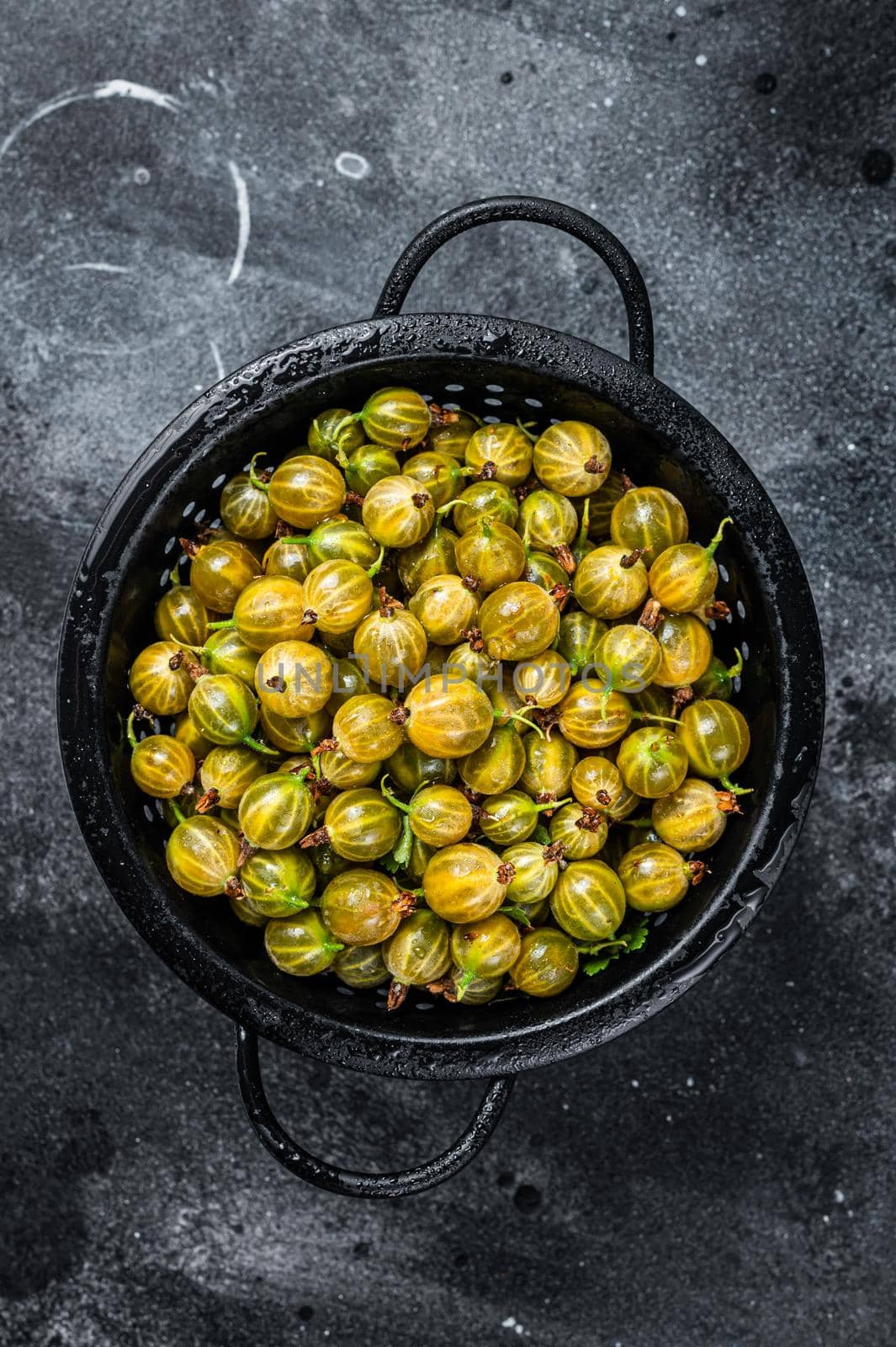 Fresh green gooseberries in a colander. Black background. Top view.