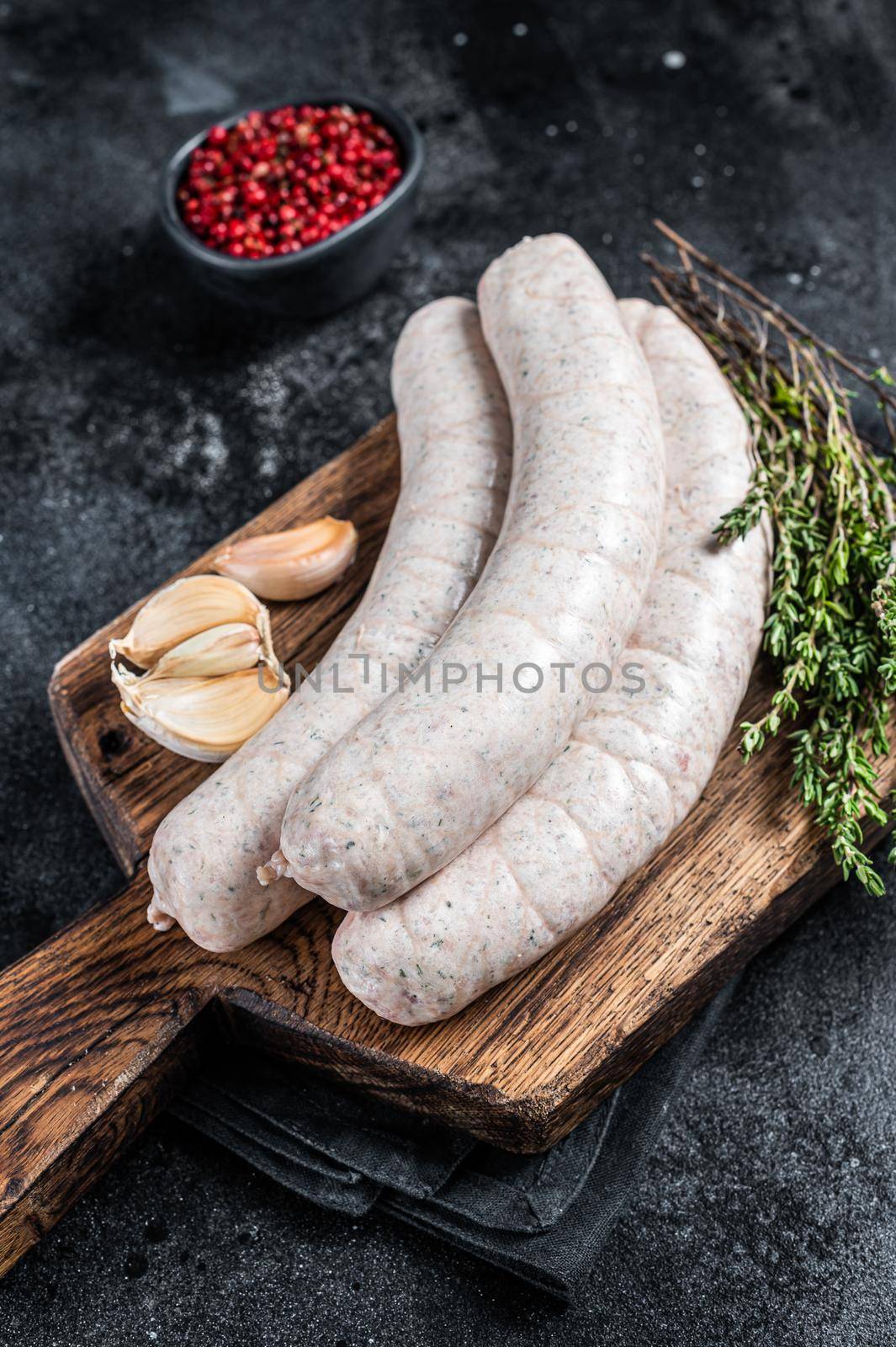 Raw Munich white sausage weisswurst on wooden board. Black background. Top view.