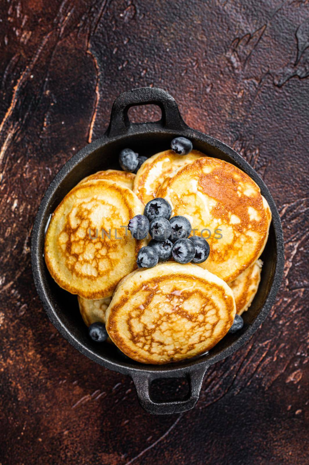 Fried Pancakes with fresh blueberries and maple syrup in a pan. Dark background. Top View.
