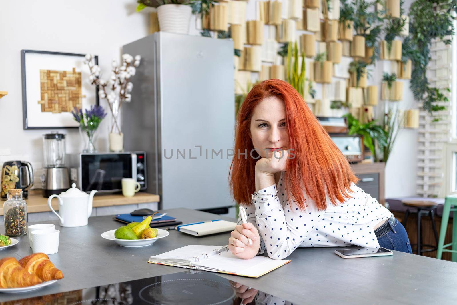 attractive caucasian woman writing in paper notebook on the kitchen table in the kitchen at home. beautiful woman write recipes. Concept of housekeeping, recipe, planning.