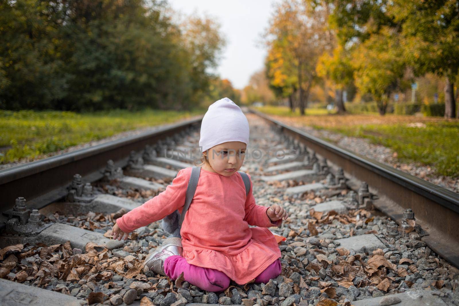 little girl sitting on the railroad tracks. toddler plays on railroad in forest